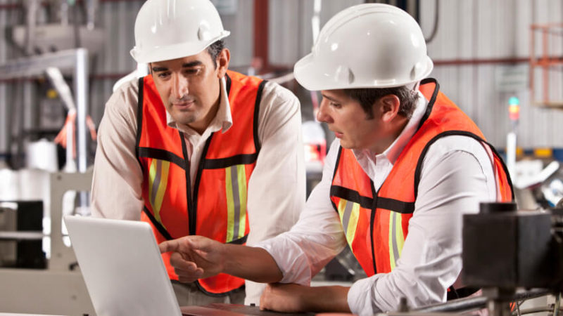 Two workers in hard hats discussing something on a laptop