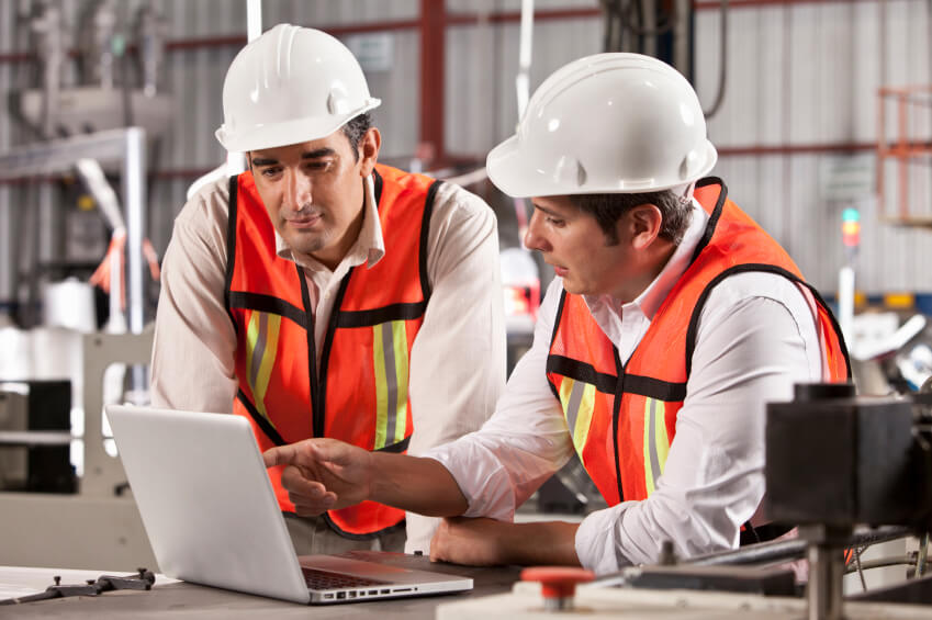 Two workers in hard hats discussing something on a laptop