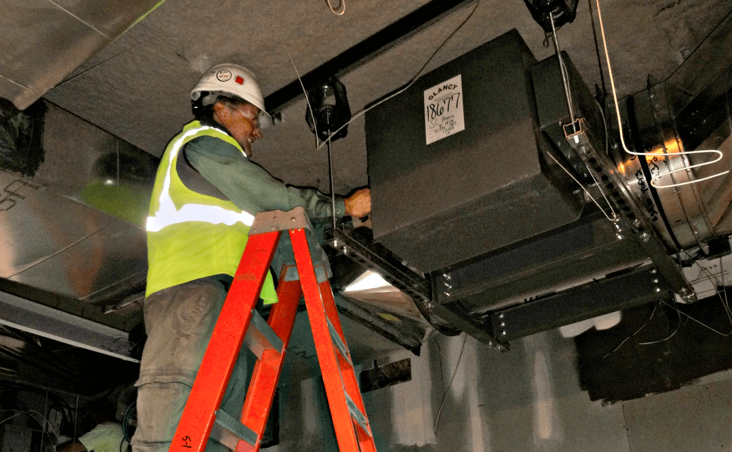 A worker standing on a ladder and working on a heating unit